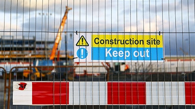 Construction site safety barriers and signage with a crane in the background